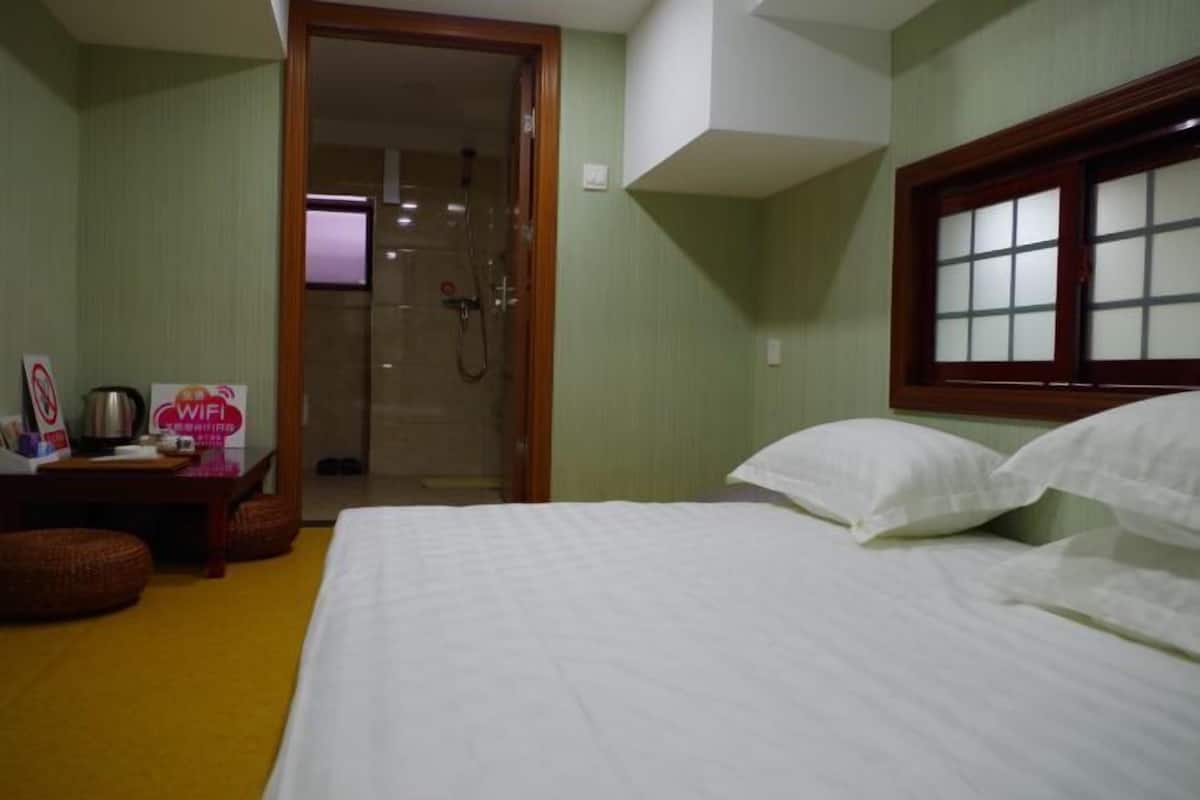 A hotel room with a bed, a window, a shower area, and a sign indicating WiFi availability.