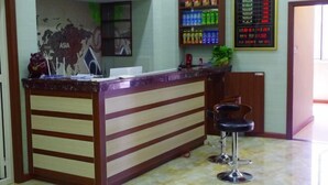 Mostrador de recepción con un mural de un mapa mundial, un tablón de anuncios con precios y una zona de bar con taburetes.