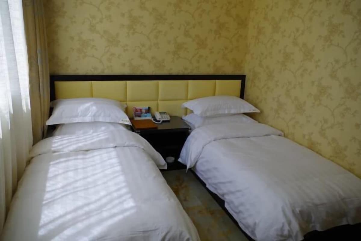 A hotel room with two single beds, a nightstand with a telephone, and a headboard.