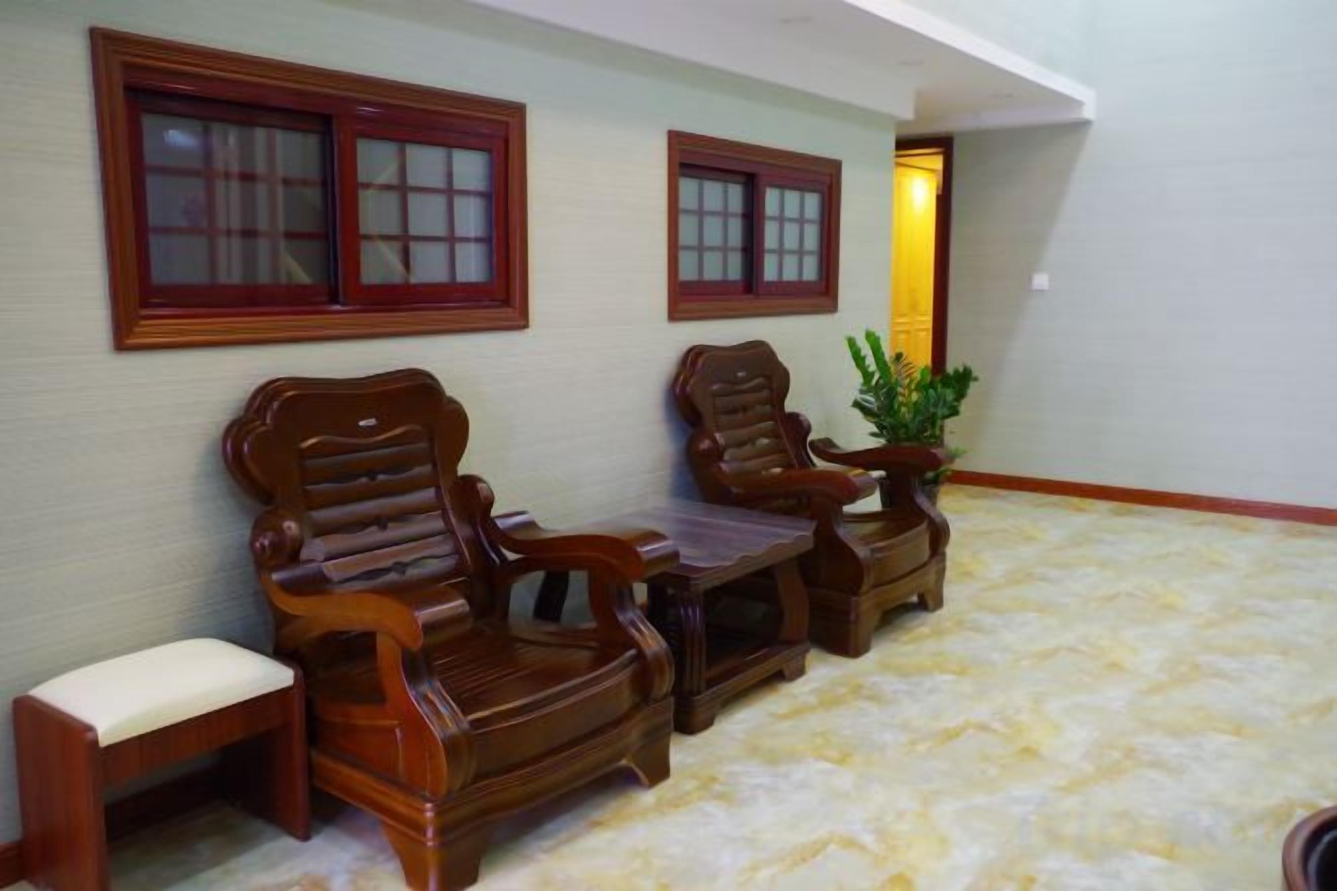 A room with two wooden chairs and a small table, a potted plant, and a window with a red frame.