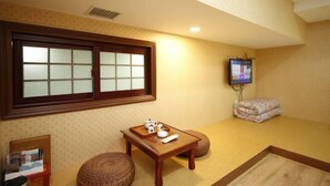 Una habitación con un ventanal grande, una mesita de madera con un juego de té, un televisor y un pouf tejido.