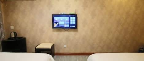 A hotel room with two beds, a flat-screen TV mounted on the wall, a small table with a kettle, and a wall-mounted air conditioner.