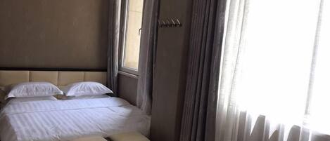 Une chambre d’hôtel avec un lit, un banc, une fenêtre et des rideaux.