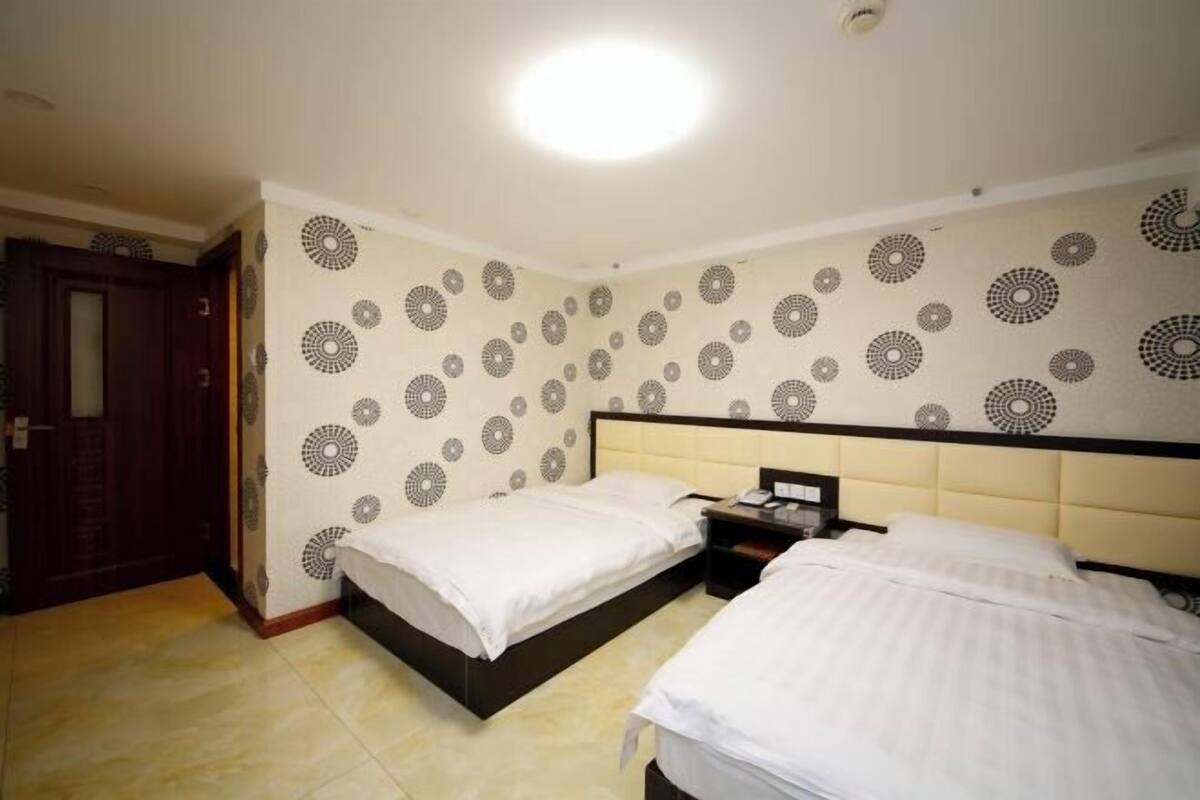 A hotel room with two beds, a nightstand, a wall with a circular pattern, and a door.