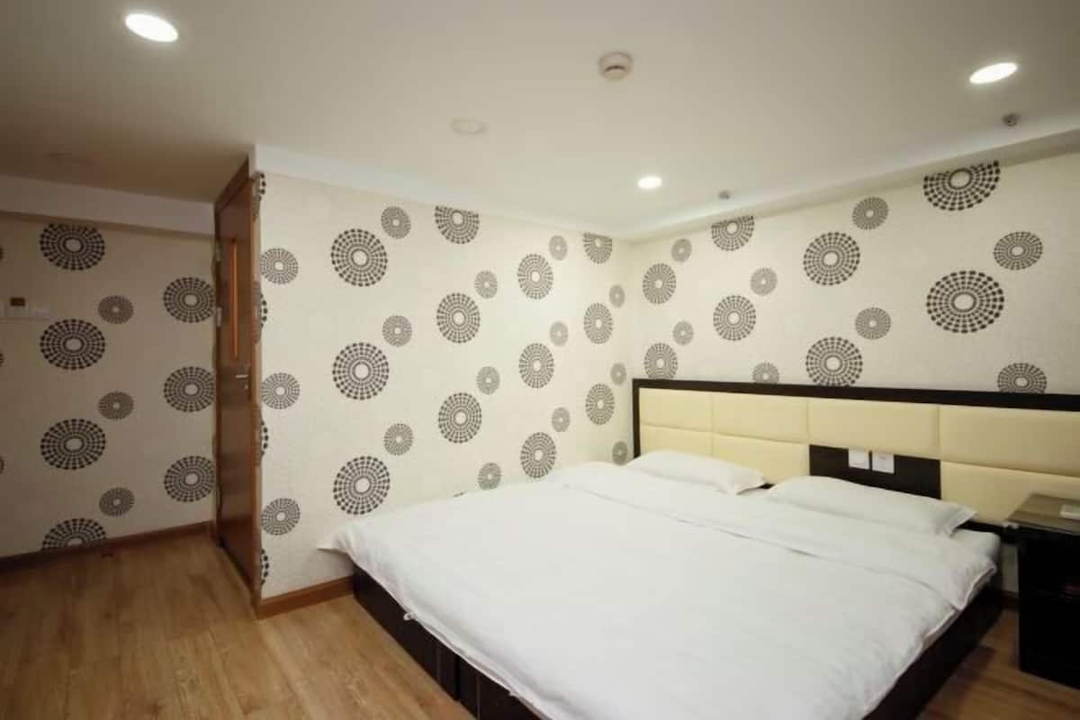 A bedroom with a bed, a headboard, and patterned wallpaper.