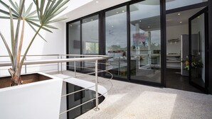 Un intérieur moderne avec une porte vitrée donnant sur un espace repas, un escalier doté d’une rampe en métal et une plante en pot.