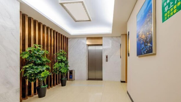 A modern hotel lobby with a marble floor, a reception desk, potted plants, a wall-mounted elevator, and a large painting on the wall. - Guangzhou Manya Fashion Hotel (Guangzhou)