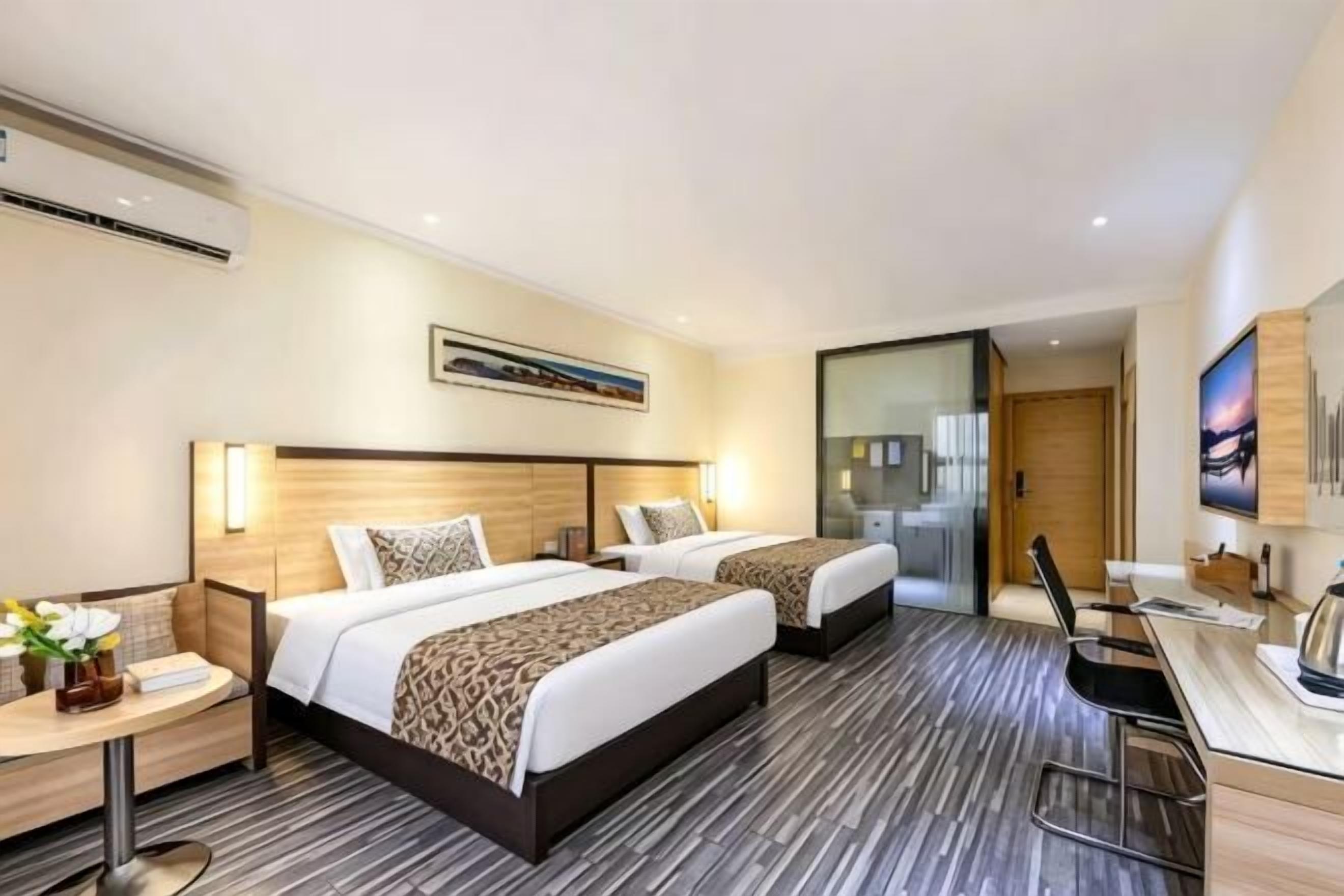 Quarto de hotel com duas camas, uma escrivaninha, uma cadeira, uma televisão e uma janela.