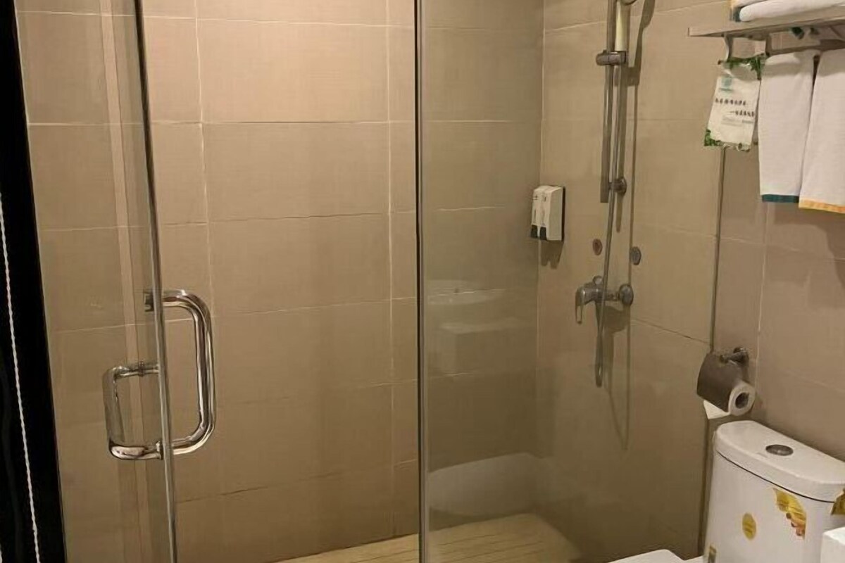 A glass-enclosed shower area with a handrail, a toilet with a paper towel dispenser, and a towel rack with a towel.