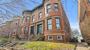 A corner building with a brick facade, multiple windows, and a green door. - Beautiful Green-Door Brownstone (Jersey City)