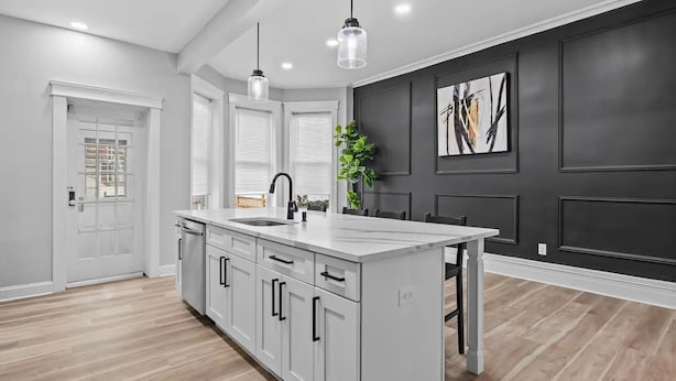 A modern kitchen with a central island, white cabinetry, and a dark accent wall. - Beautiful Green-Door Brownstone (Jersey City)