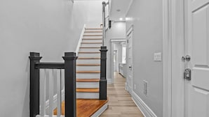 A modern hallway with a wooden staircase, white walls, and a light-colored floor. - Beautiful Green-Door Brownstone (Jersey City)