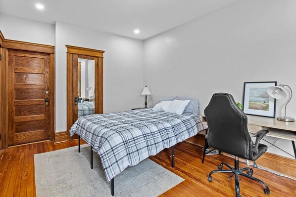 A bedroom with a bed, a desk, a chair, a lamp, and a framed picture on the wall. - Beautiful Green-Door Brownstone (Jersey City)