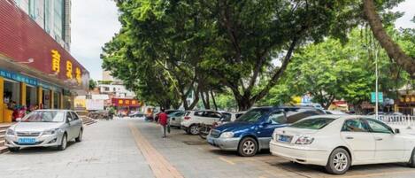 A street lined with parked cars and trees, with buildings on the left.