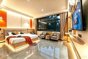 Una habitación de hotel moderna con una cama grande, televisión, zona de estar y un amplio ventanal.