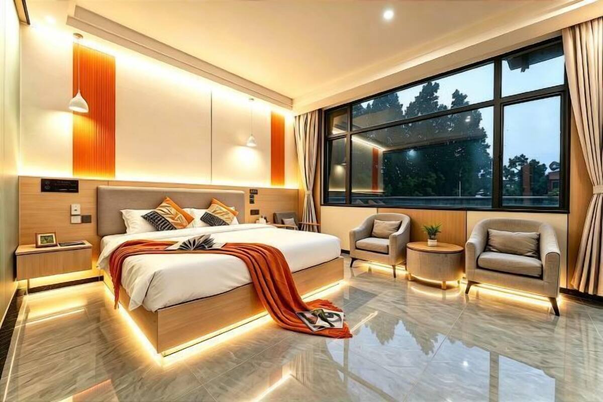 A modern bedroom with a large bed, bedside tables, a nightstand, a chair, a small table, and a large window.
