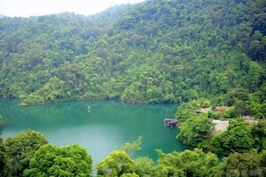 A lake surrounded by dense forest, a small building near the water, and a hill in the background.