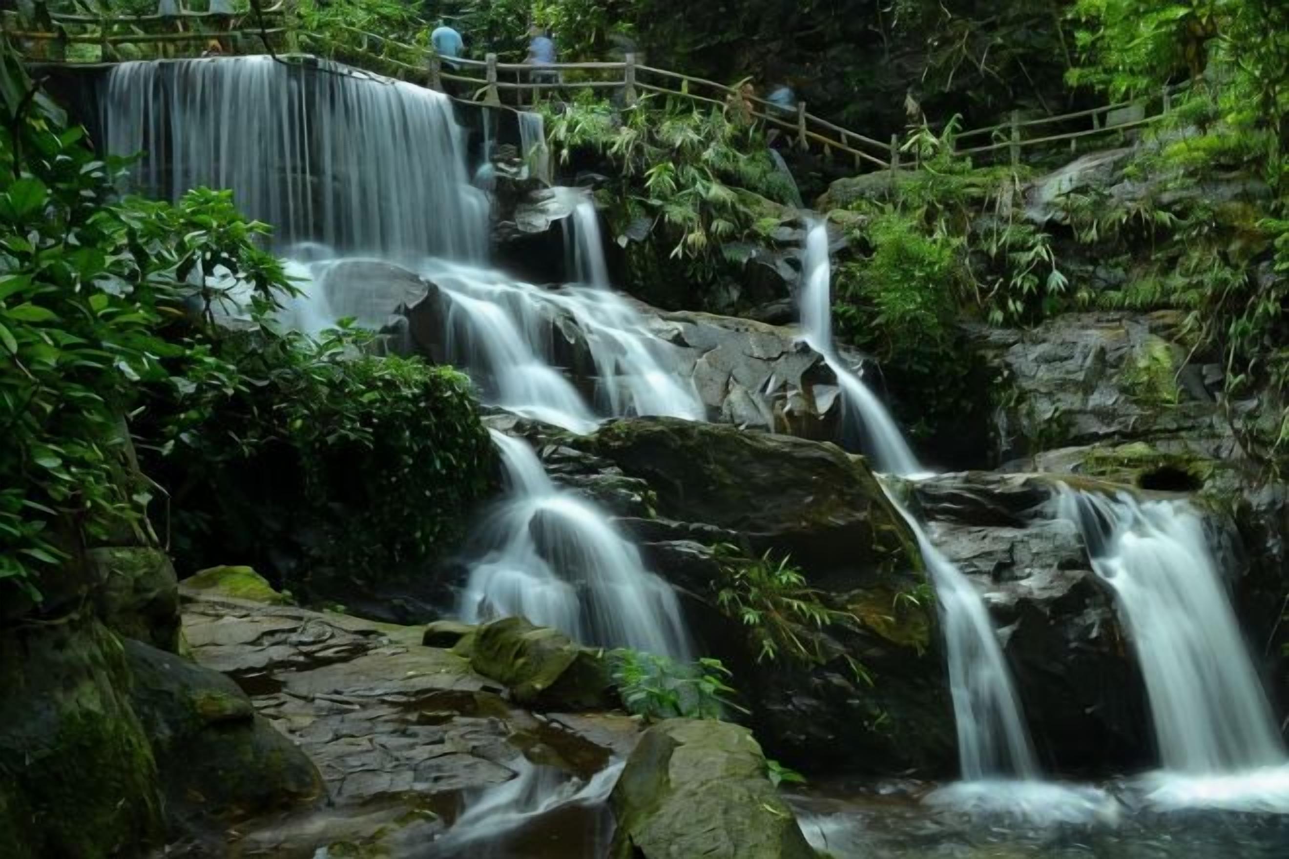 Une cascade d’eau qui dévale des rochers, avec un pont en bois en contrebas.