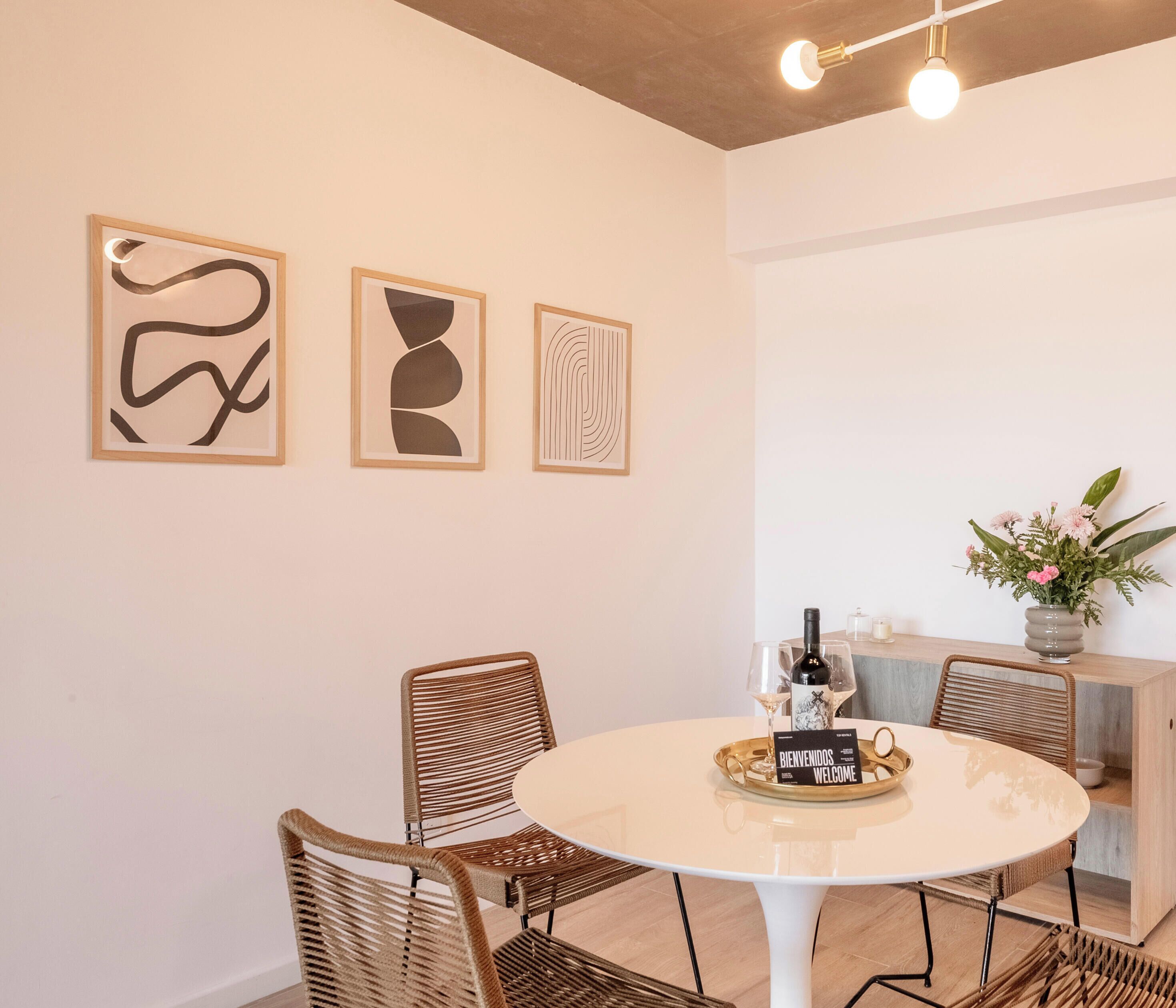 A dining area with a round table, wicker chairs, and abstract art on the wall.