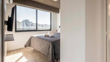 Een slaapkamer met een groot raam, een bed, een flatscreen-tv en een luchtverkoeler aan het plafond.