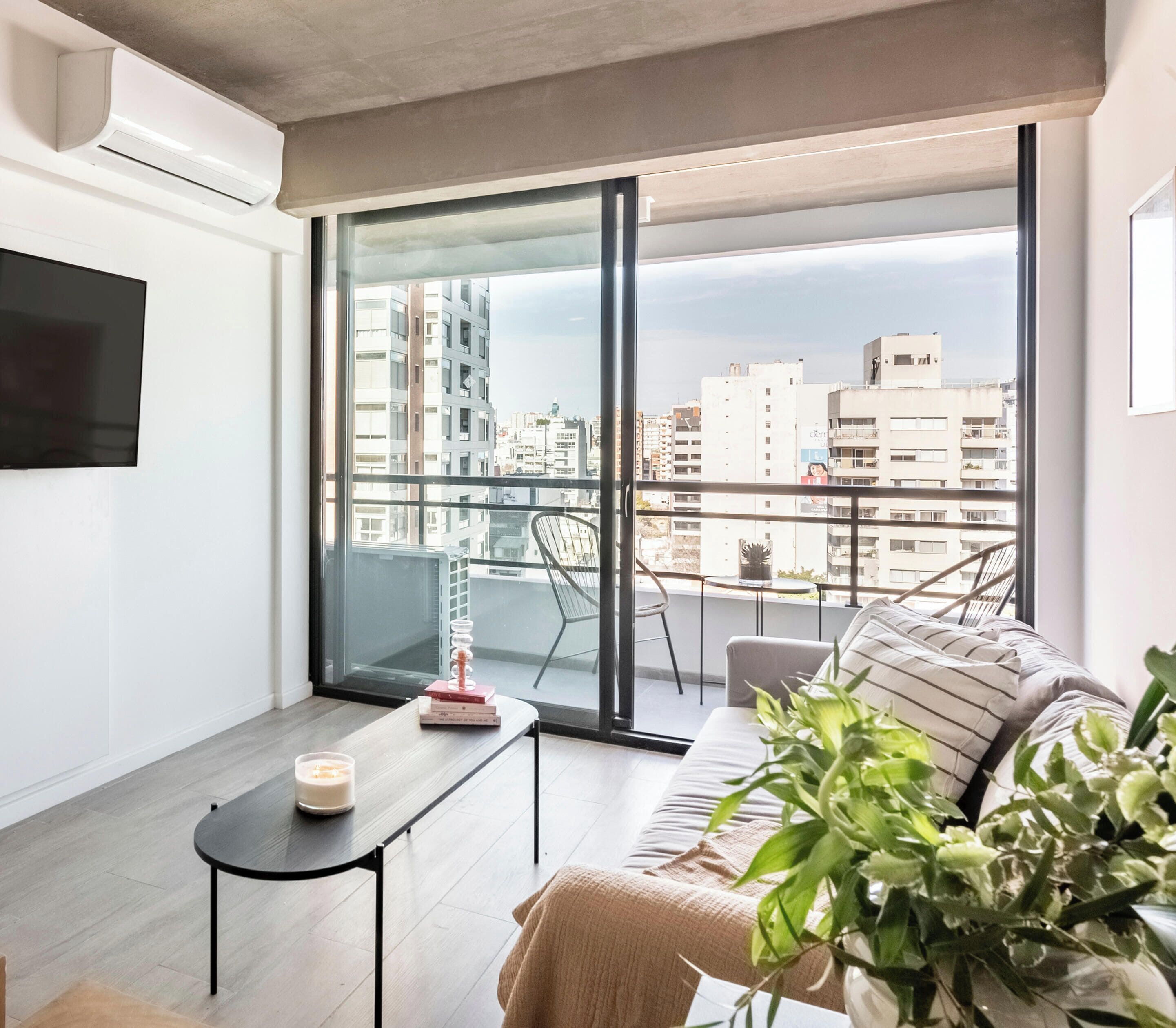 Eine moderne Wohnung mit großem Balkon, einer Couch, einem kleinen Tisch mit Kerze und einem Topf mit Pflanze.