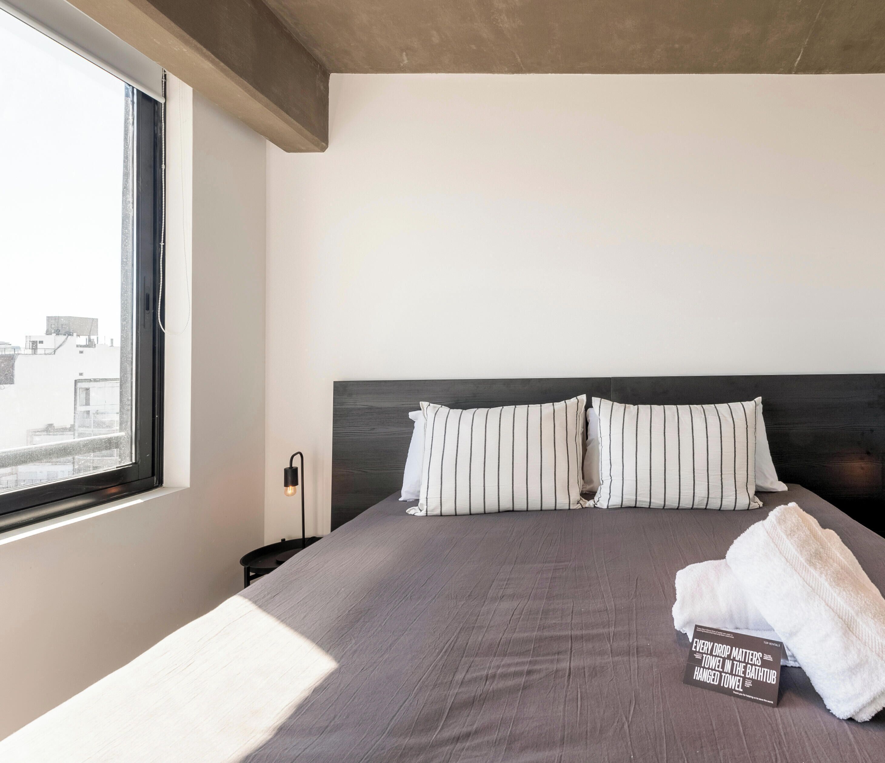 A hotel room with a large bed, striped pillows, a bedside table with a lamp, and a towel on the bed.