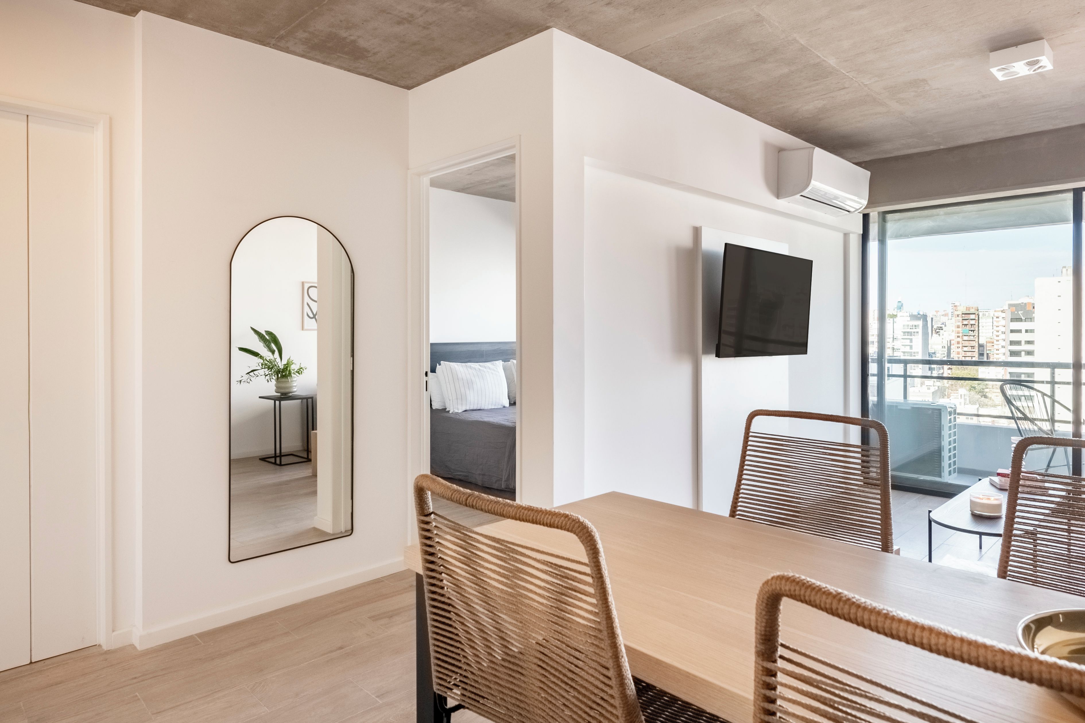 Habitación de hotel moderna con zona de comedor, un espejo grande, televisor de pantalla plana y balcón con vistas a la ciudad.
