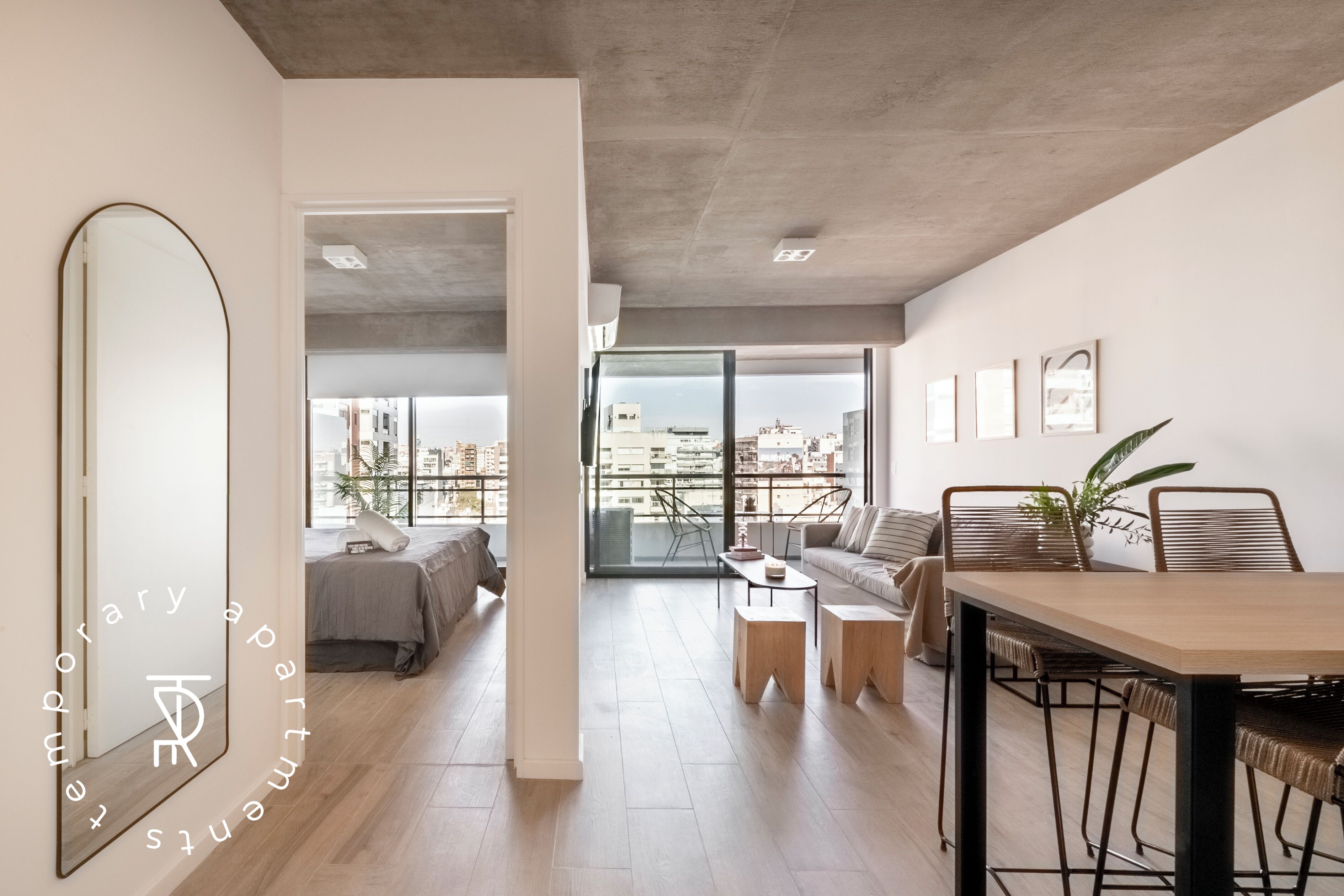 A modern apartment with a large mirror, a dining area, a sofa, and a balcony with city views.