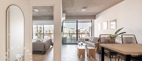 A modern apartment with a large mirror, a dining area, a sofa, and a balcony with city views.