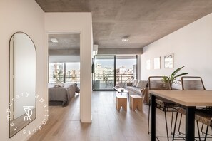 Un apartamento moderno con un espejo grande, comedor, sofá y balcón con vistas a la ciudad.