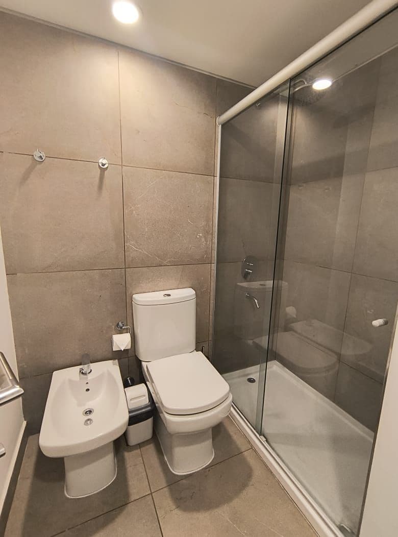 Un baño con inodoro, bidé y zona de ducha con mampara de vidrio.
