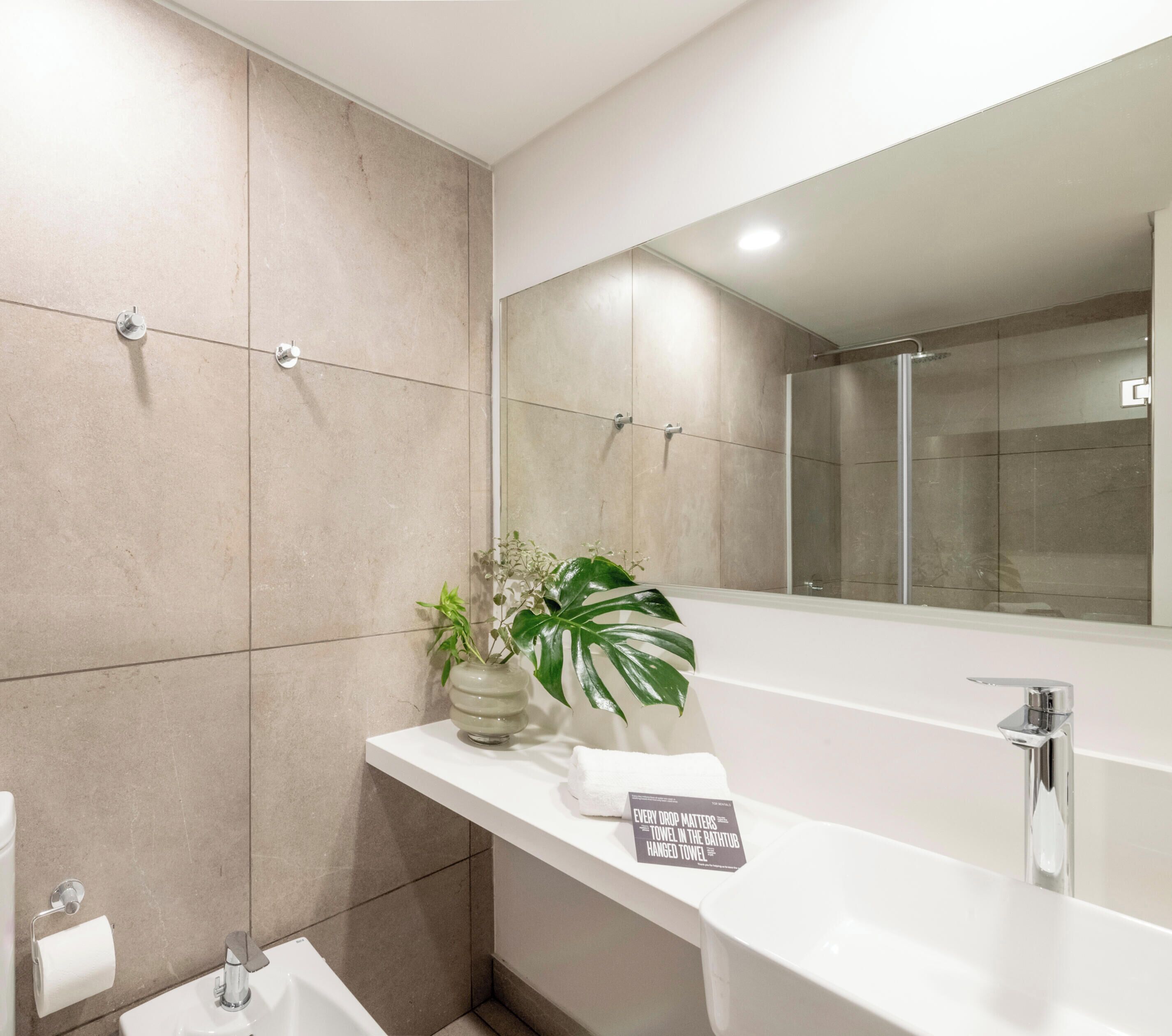 A modern bathroom with a large mirror, a bathtub, a sink, and a potted plant.