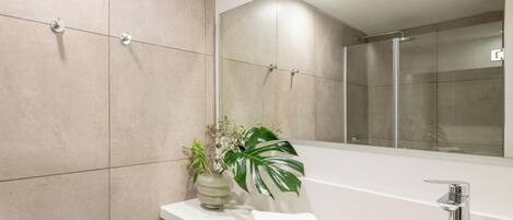 A modern bathroom with a large mirror, a bathtub, a sink, and a potted plant.