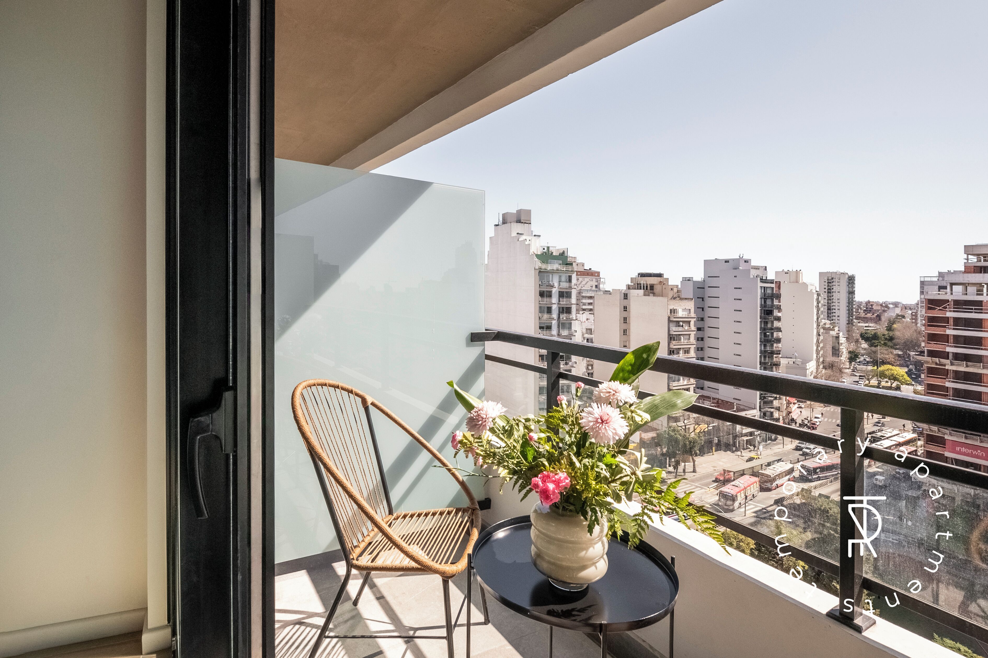 A balcony with a wicker chair, a small round table, and a vase of flowers.