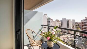 A balcony with a wicker chair, a small round table, and a vase of flowers.