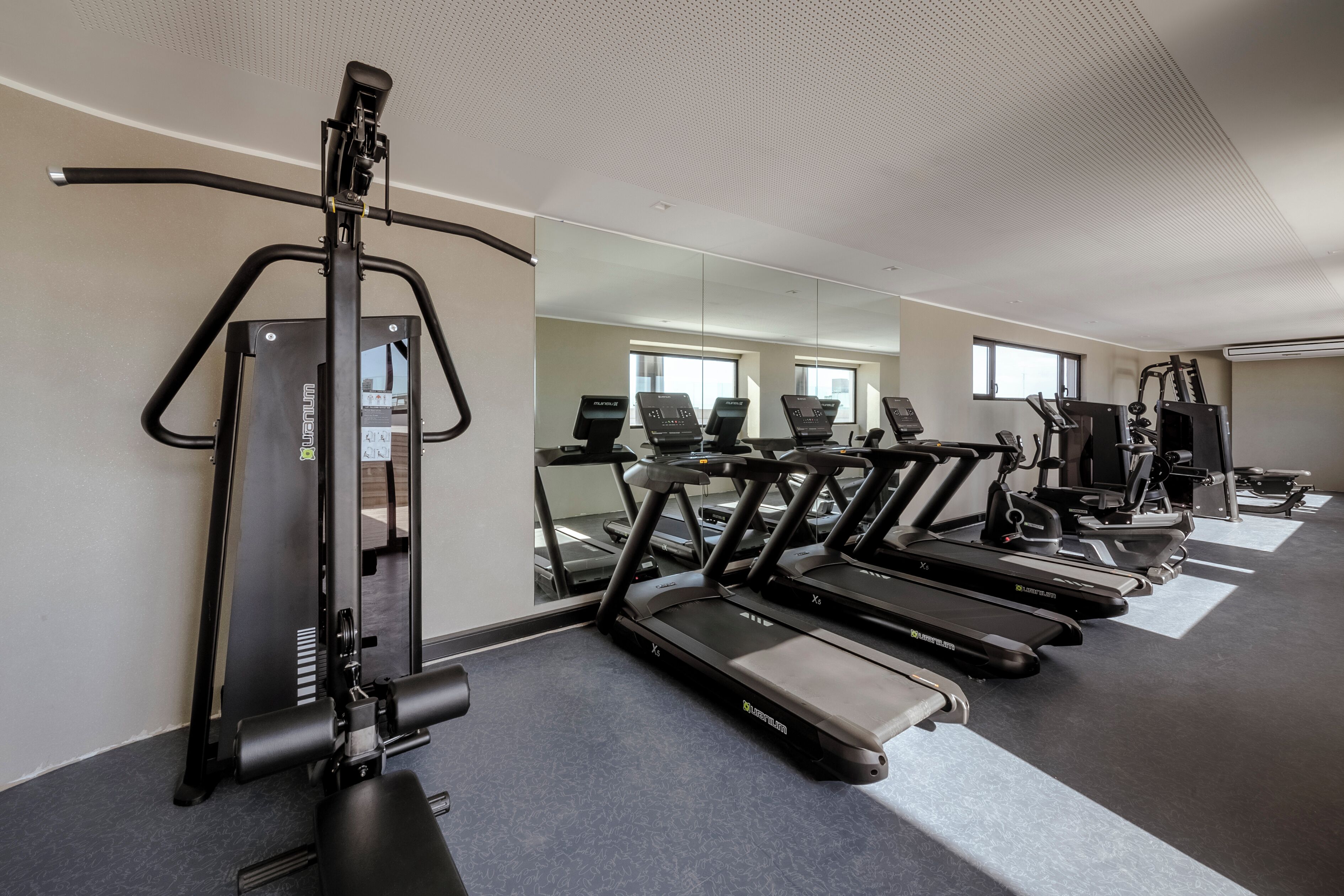 Un gimnasio con cintas de correr, máquinas de pesas y espejos en las paredes.