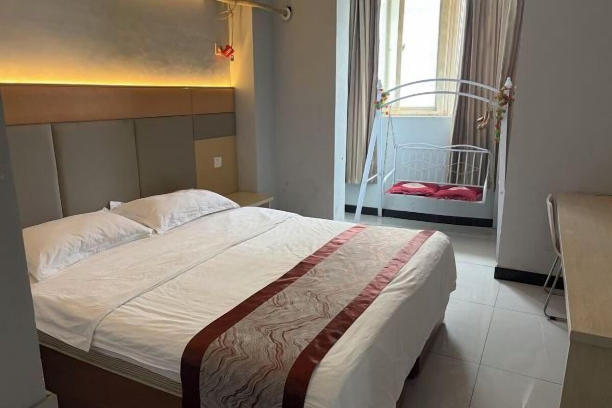 Quarto de hotel com cama, mesa de cabeceira, uma cadeira e janela com cortinas.