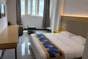 Ett hotellrum med en säng, ett skrivbord, en stol, ett litet bord och en TV.