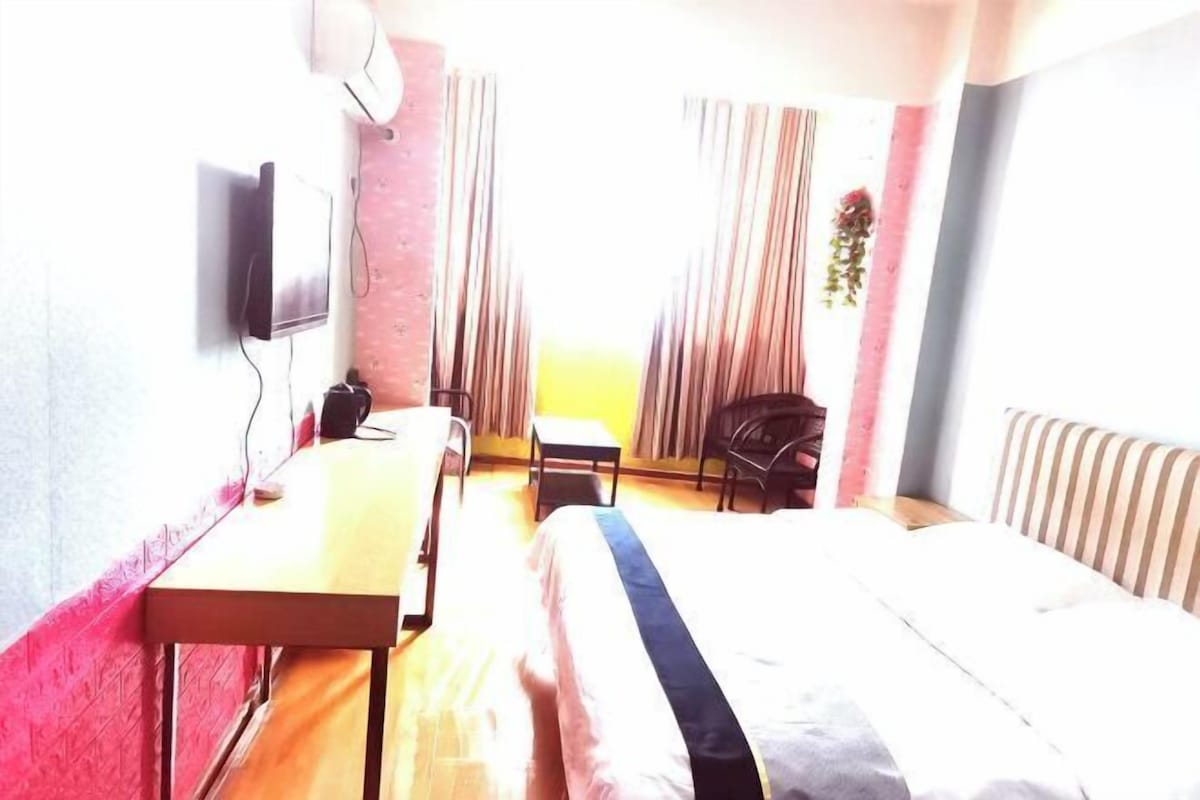 Ein Hotelzimmer mit einem Bett, einem Schreibtisch, einem Stuhl, einem Fernseher und Vorhängen.