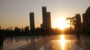 Een ruim, open plein met een ondergaande zon en hoge gebouwen.
