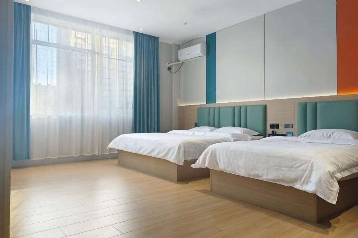 Habitación de hotel con dos camas, un amplio ventanal con cortinas, aire acondicionado instalado en la pared y diseño moderno.