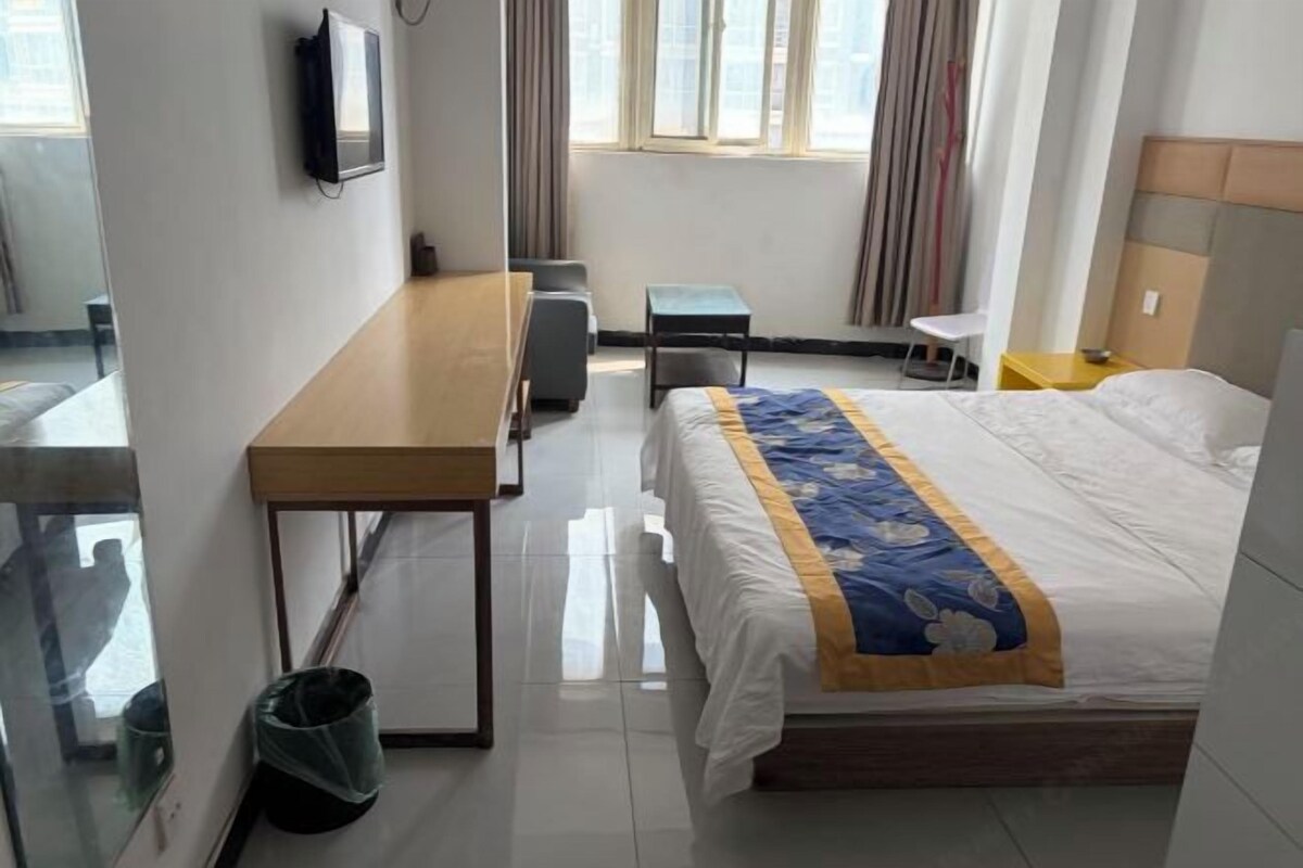 Une chambre d’hôtel comprenant un lit, un bureau, une chaise, une petite table, une poubelle et une fenêtre avec des rideaux.