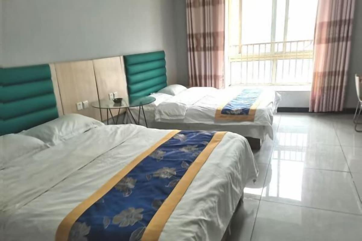 Ein Hotelzimmer mit zwei Betten, einem kleinen Tisch und einem Fenster mit Vorhängen.