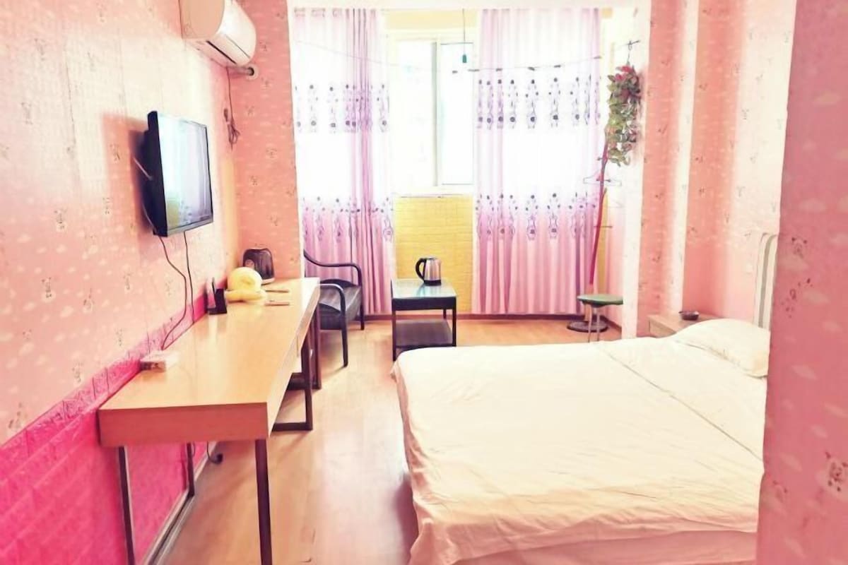 Ein Hotelzimmer mit Bett, Schreibtisch, Stuhl, Fernseher und einem fensterbepflanzten Fenster.