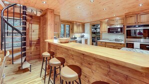 A wooden cabin interior with a kitchen, bar area, and spiral staircase. - Luxe Smoky Mountains Cabin w/ Hot Tub & Views! (Waynesville)