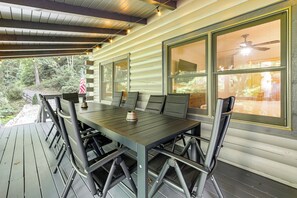 Un espace extérieur abrité, aménagé pour les repas, avec une longue table et des chaises, de grandes fenêtres et un drapeau américain.
