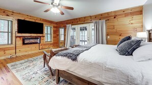 A wooden-paneled bedroom with a bed, a television mounted on the wall, and a fireplace. - Luxe Smoky Mountains Cabin w/ Hot Tub & Views! (Waynesville)