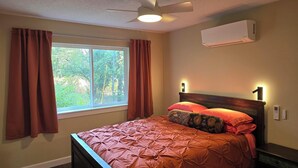 Ein Schlafzimmer mit Bett, Fenster, Vorhängen, einer Klimaanlage und einem Deckenventilator.