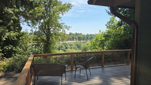 Eine Holzterrasse mit Metallgeländer, zwei Korbstühle und Blick auf eine bewaldete Landschaft.