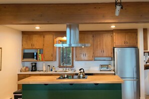 A modern kitchen with wooden cabinets, a stainless steel refrigerator, a microwave, and a large island with a kettle. - Torch lake waterfront:100 ft of sandy beach, 3-bedroom, 3-bath cottage (Alden)